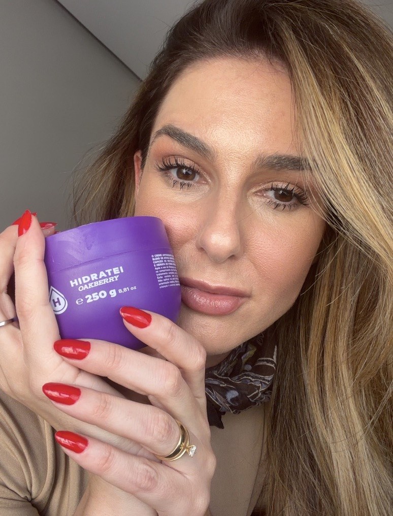 Aline segura o pote de Hidratei Oakberry junto ao rosto